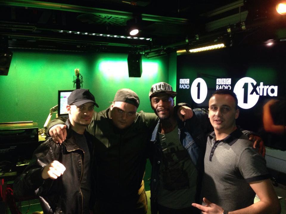 Michael Darius Eastwood with the broadcaster Charlie Sloth and two artists inside the BBC Radio 1 and 1Xtra studio, the station logos on the wall